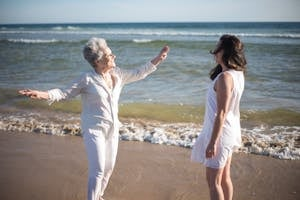 Joyful elderly mother and adult daughter bonding on a sunny beach day in Portugal.